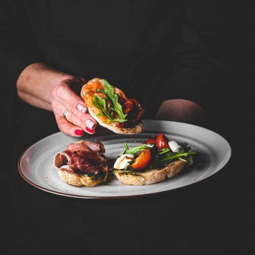 chef in a black suit holds in his hands plate with Bruschetta on